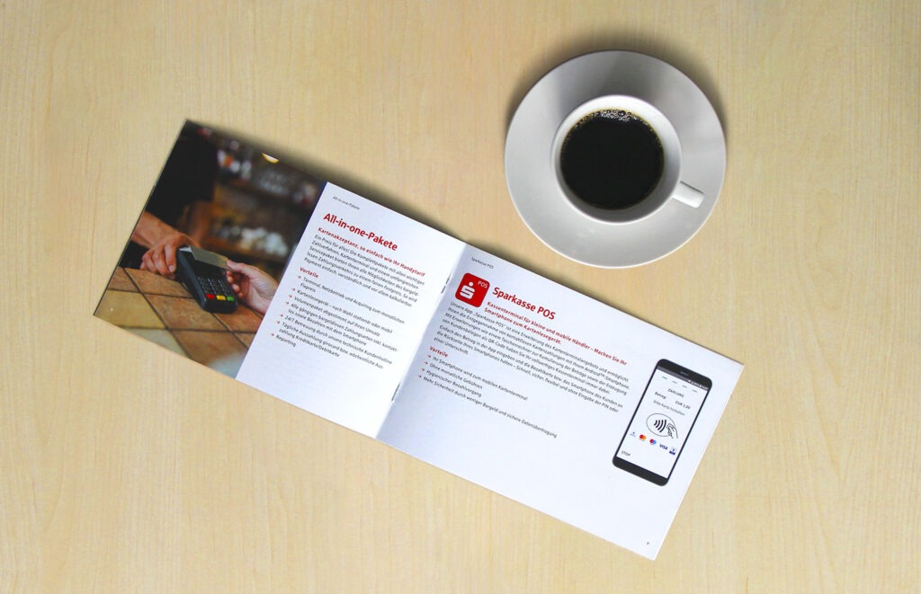 Aufgeschlagene Payment-Broschüre neben einer Kaffeetasse